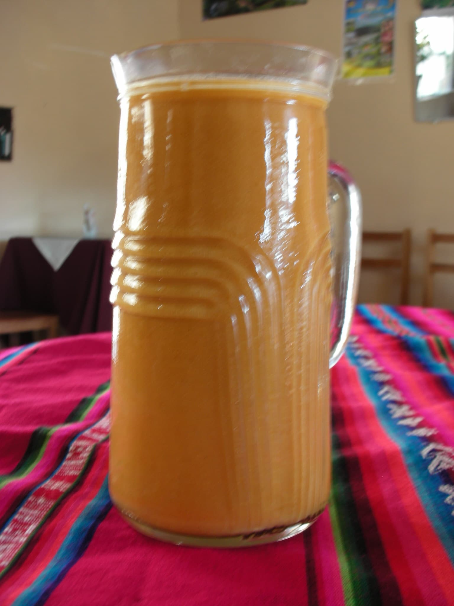 Jarra de cristal con chicha de jora dorada, sobre mantel andino de colores