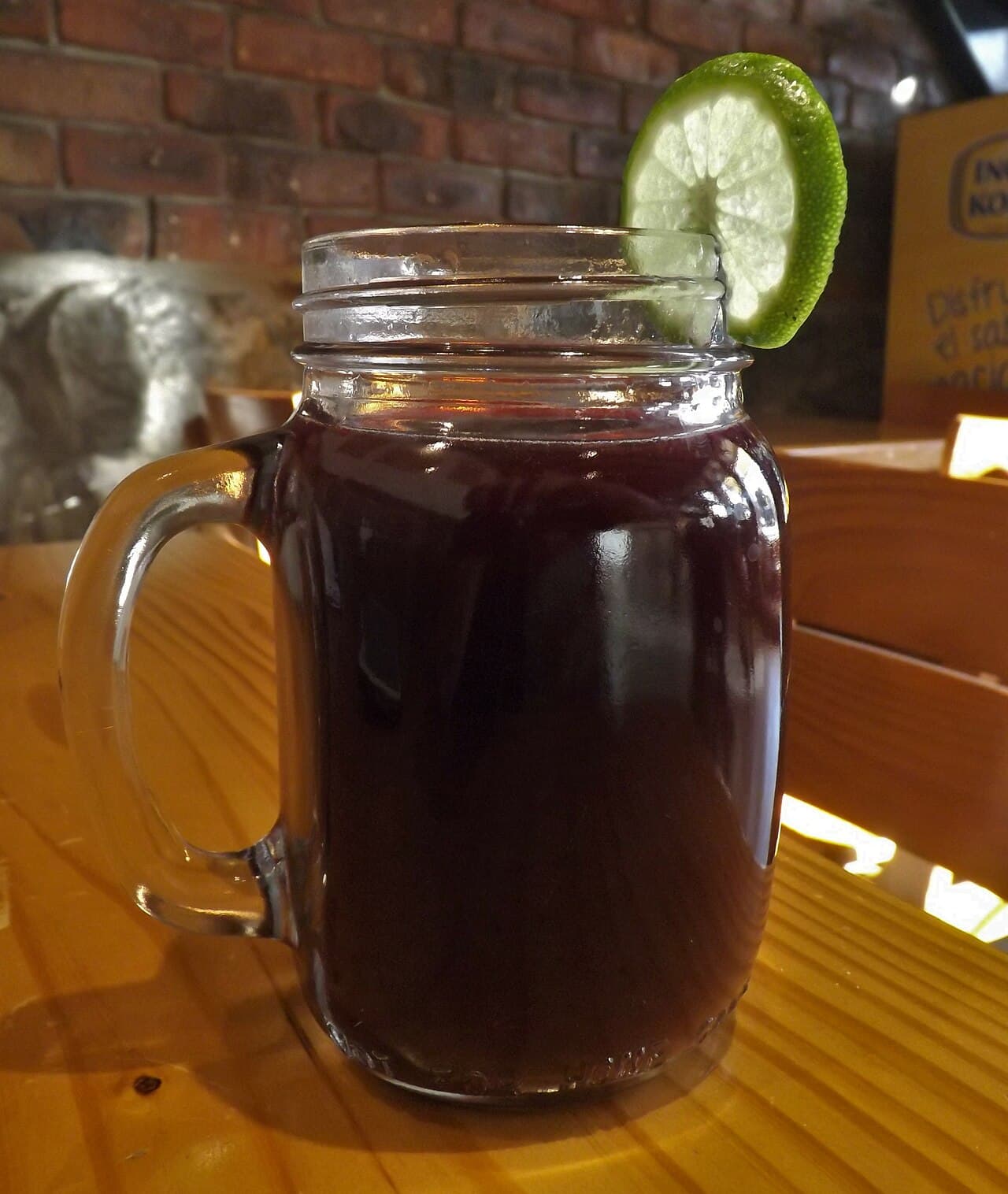 Jarra de chicha morada con rodaja de lima fresca, sobre mesa de madera