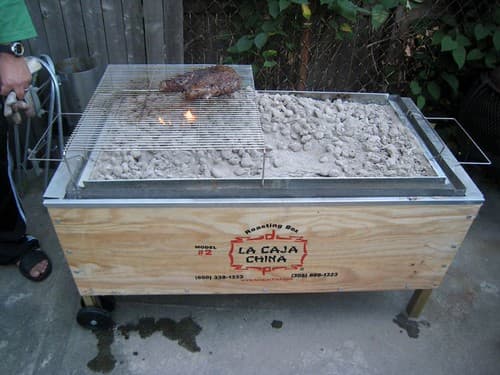 Caja china con brasas blancas repartidas sobre la tapa metálica